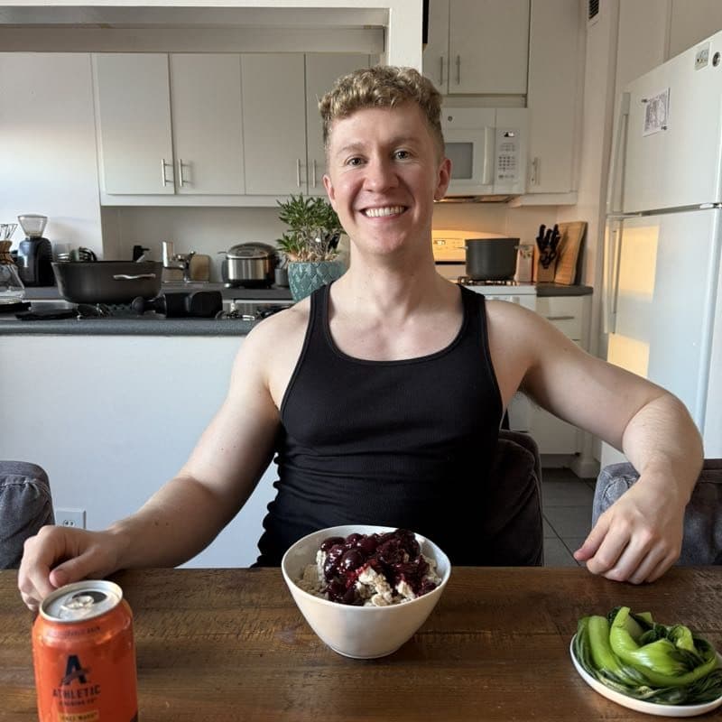 Brett smiling at his kitchen table over a bowl of oats piled with cherries, bok choy on the side