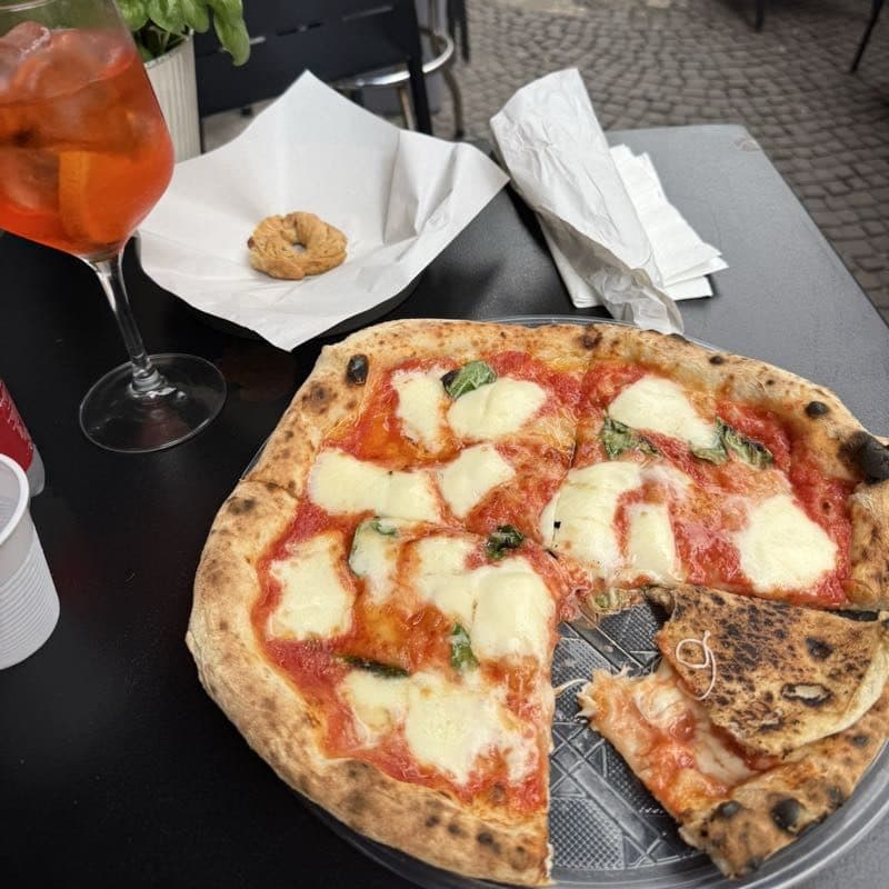 A margherita pizza with one slice already gone, next to an Aperol spritz on a cafe table