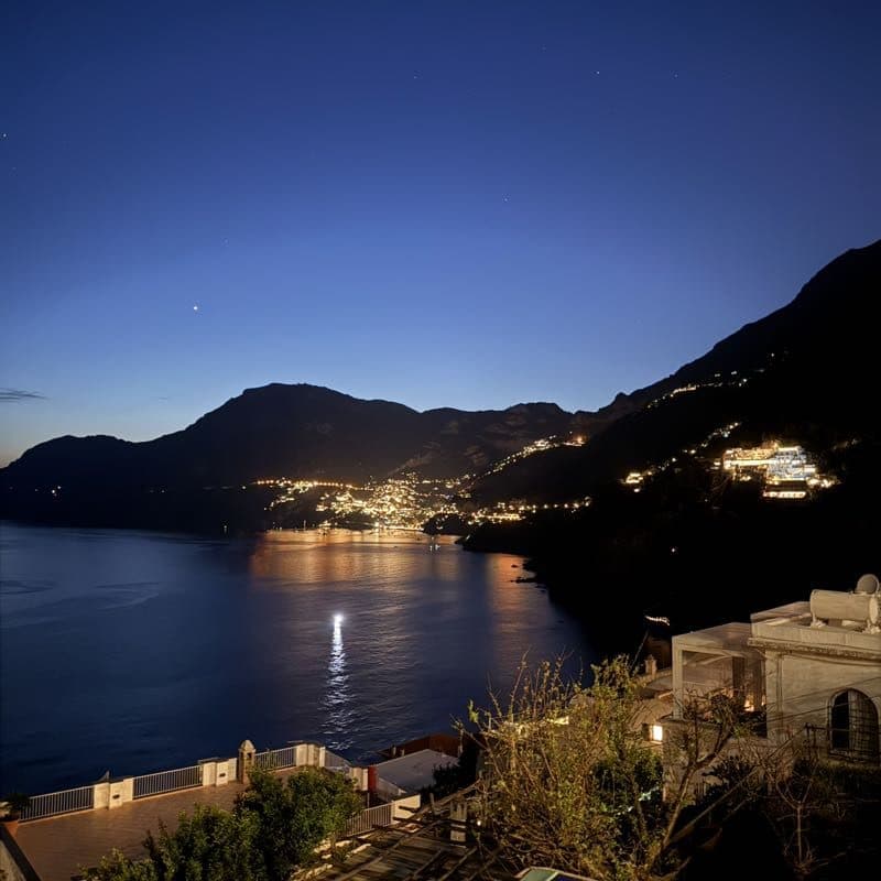 A hillside town glittering across a dark bay just after sunset